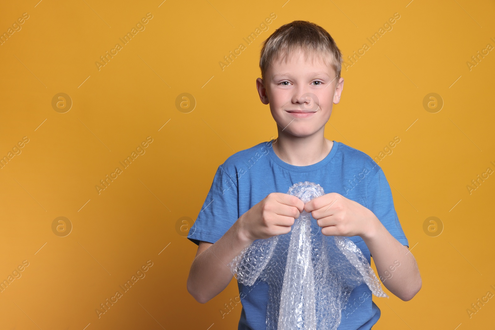 Photo of Boy popping bubble wrap on yellow background, space for text. Stress relief
