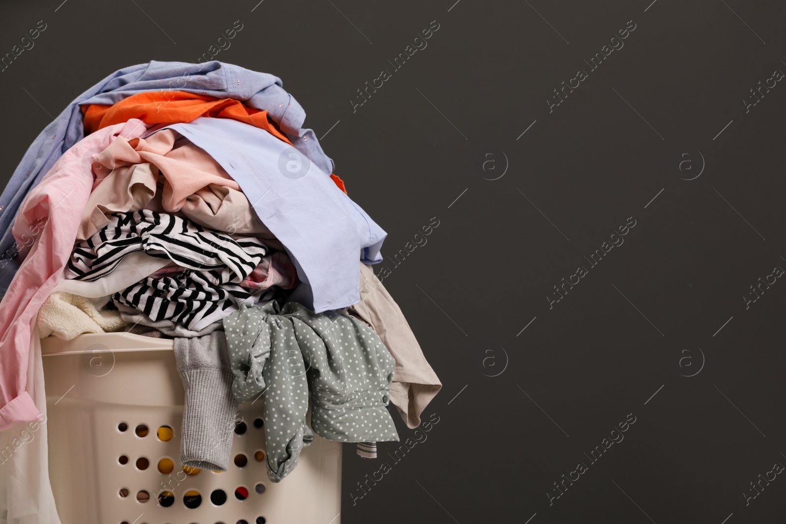 Photo of Laundry basket with clothes against dark grey background. Space for text