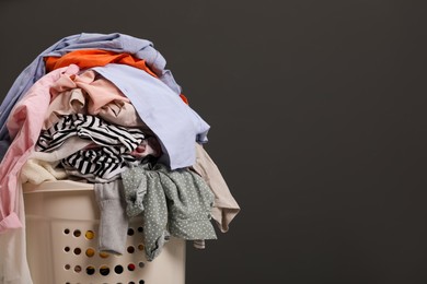 Laundry basket with clothes against dark grey background. Space for text