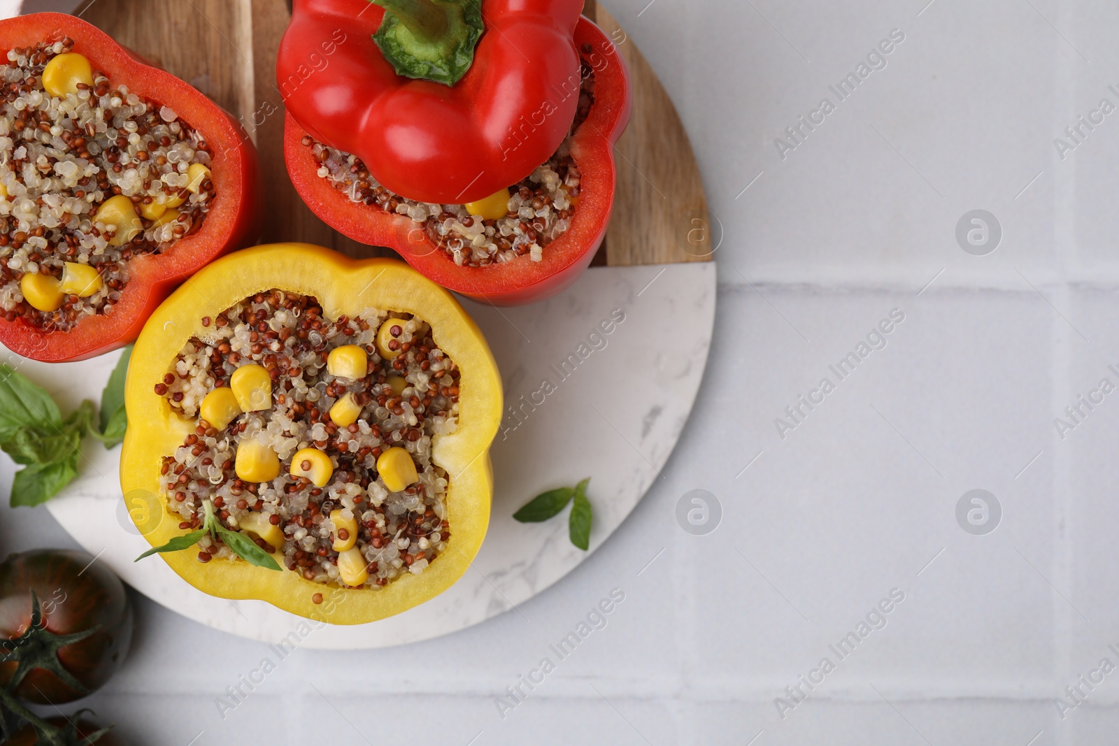 Photo of Quinoa stuffed bell peppers, tomatoes and basil on white tiled table, flat lay. Space for text