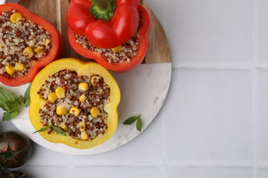 Photo of Quinoa stuffed bell peppers, tomatoes and basil on white tiled table, flat lay. Space for text