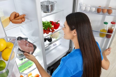 Young woman taking pack of meat out of refrigerator indoors, above view