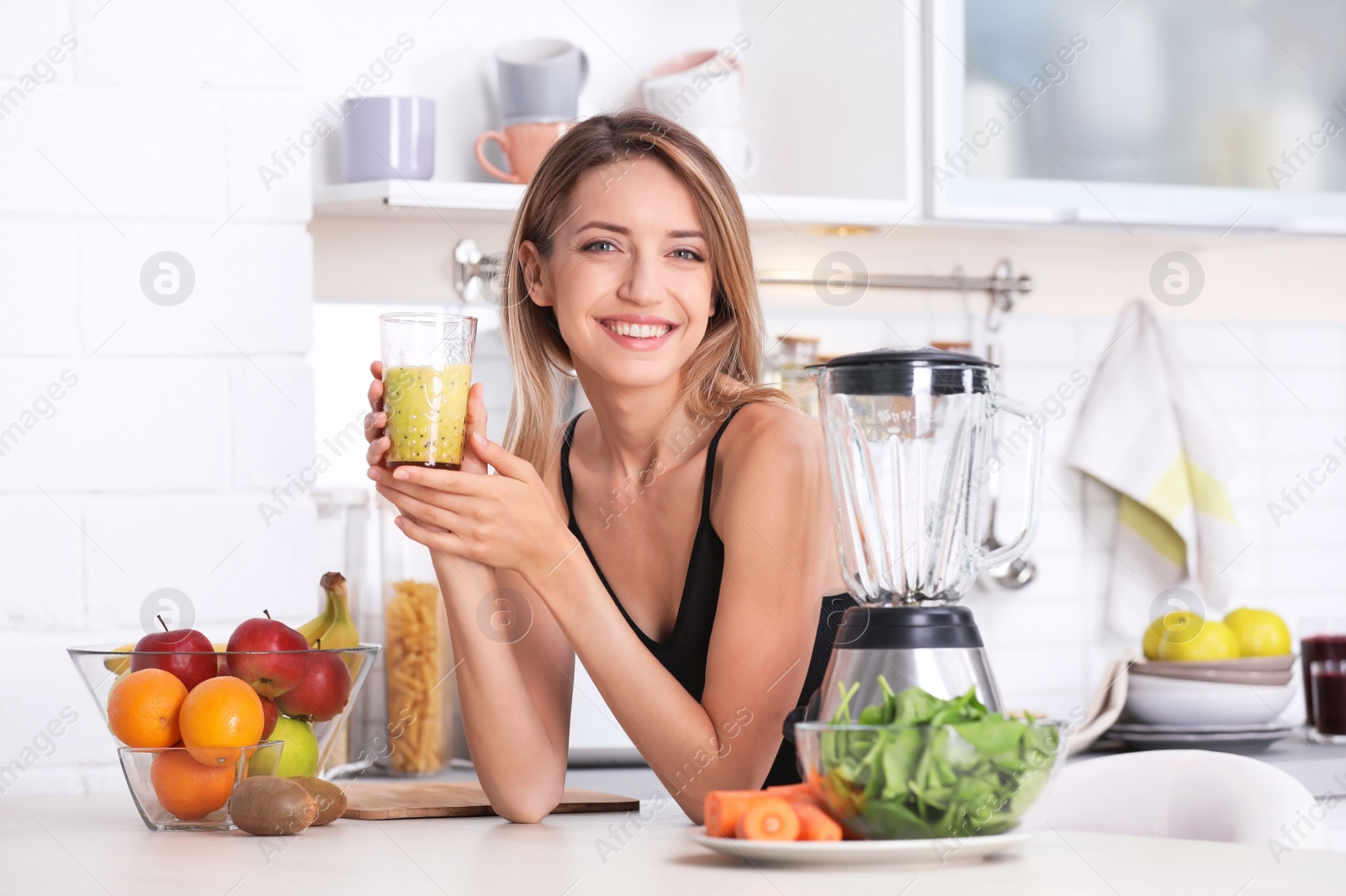 Photo of Young woman with glass of tasty healthy smoothie at table in kitchen