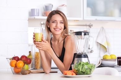 Young woman with glass of tasty healthy smoothie at table in kitchen