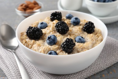 Photo of Tasty oatmeal porridge with blackberries and blueberries in bowl on table, closeup