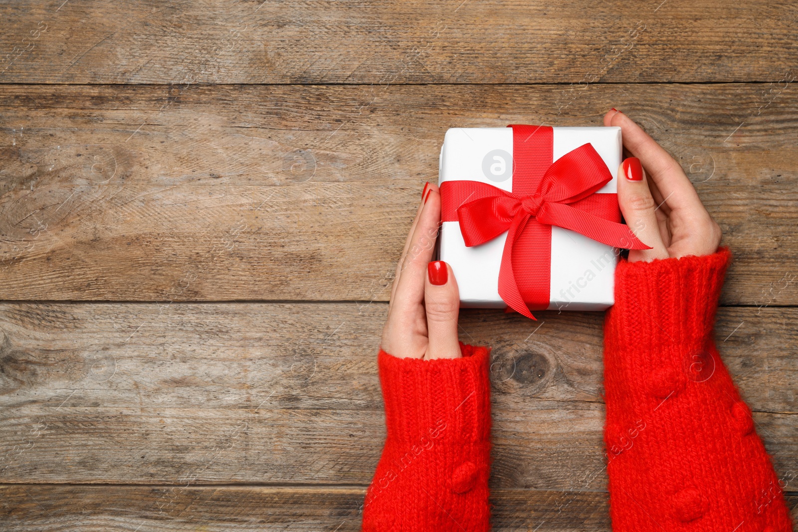 Photo of Young woman holding Christmas gift on wooden background, top view. Space for text