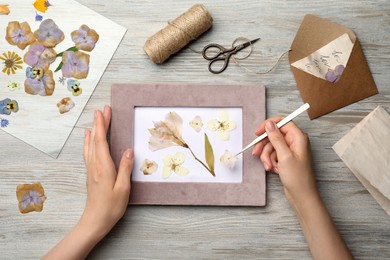 Woman making beautiful herbarium with pressed dried flower at wooden table, top view.