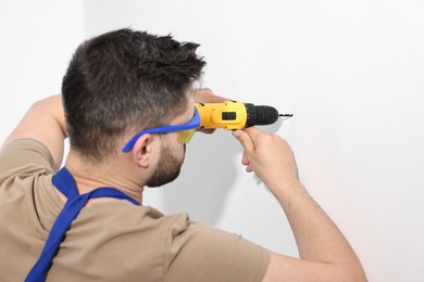 Photo of Young worker in uniform using electric drill indoors