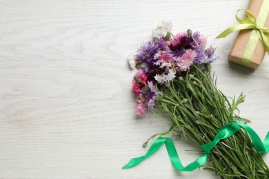 Bouquet of beautiful cornflowers and gift box on white wooden table, flat lay. Space for text