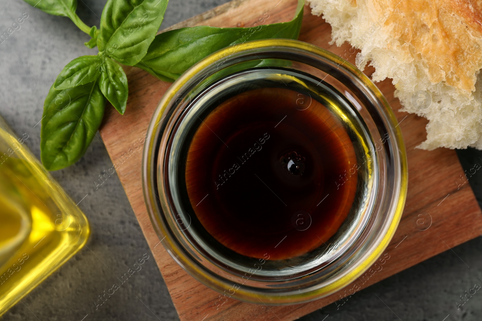 Photo of Bowl of organic balsamic vinegar with oil, basil and bread on grey table, flat lay