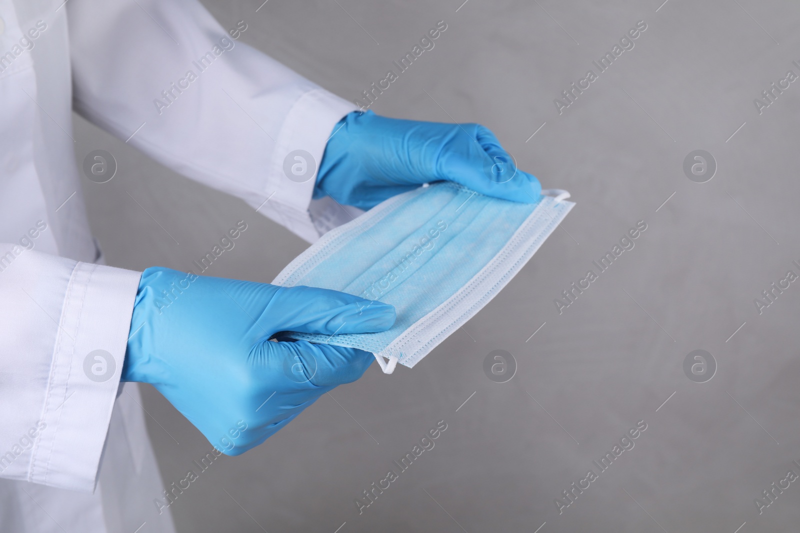 Photo of Doctor holding protective mask on light grey background, closeup