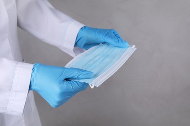 Doctor holding protective mask on light grey background, closeup