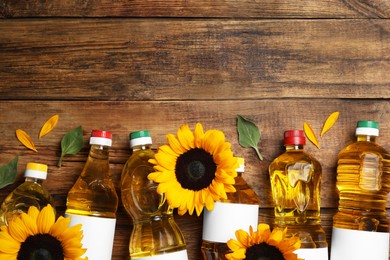 Bottles of sunflower cooking oil and beautiful flowers on wooden table, flat lay. Space for text