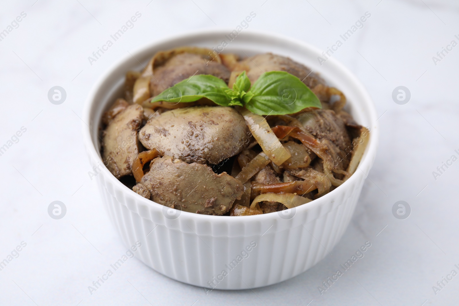 Photo of Delicious fried chicken liver with onion and basil in bowl on white table, closeup