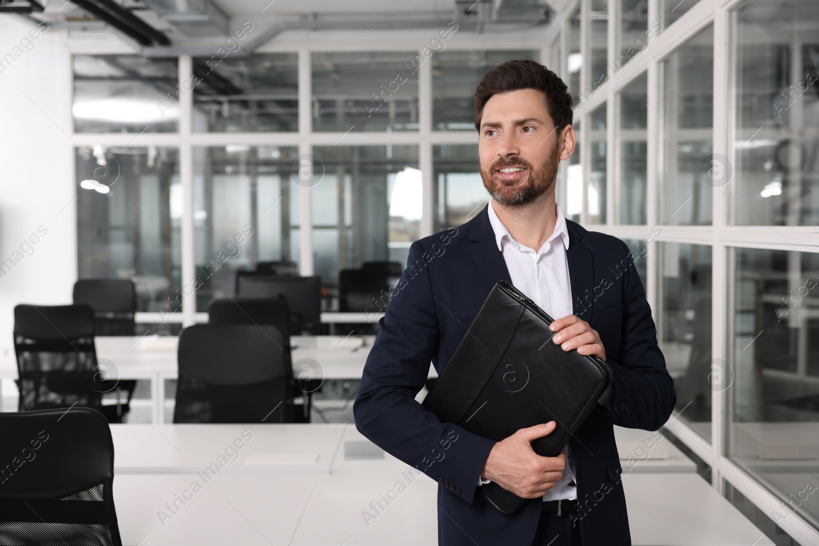 Photo of Happy real estate agent with leather portfolio indoors. Space for text