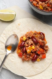 Photo of Tasty chili con carne with tortillas on light table, flat lay