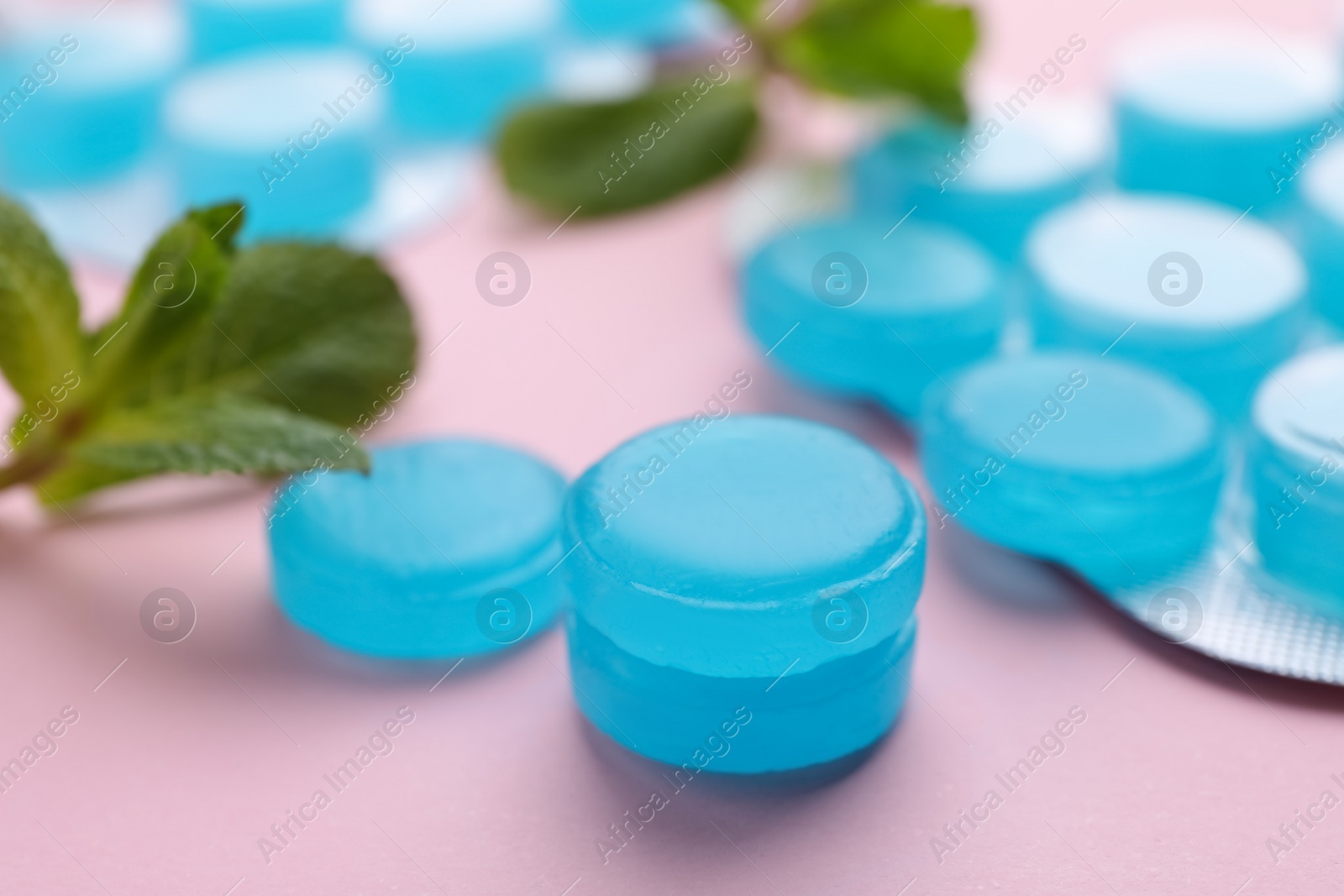 Photo of Many light blue cough drops and mint on pink background, closeup