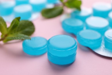 Photo of Many light blue cough drops and mint on pink background, closeup