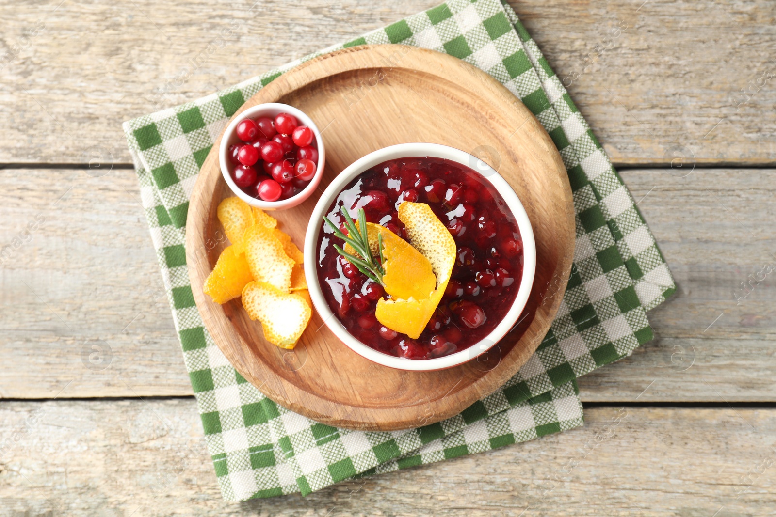 Photo of Cranberry sauce in bowl, fresh berries, rosemary and orange peels on wooden table, top view