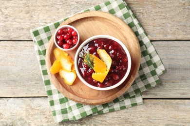 Photo of Cranberry sauce in bowl, fresh berries, rosemary and orange peels on wooden table, top view