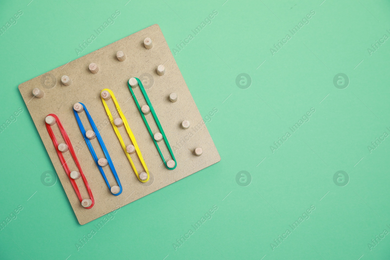Photo of Wooden geoboard with rubber bands on green background, top view with space for text. Educational toy for motor skills development