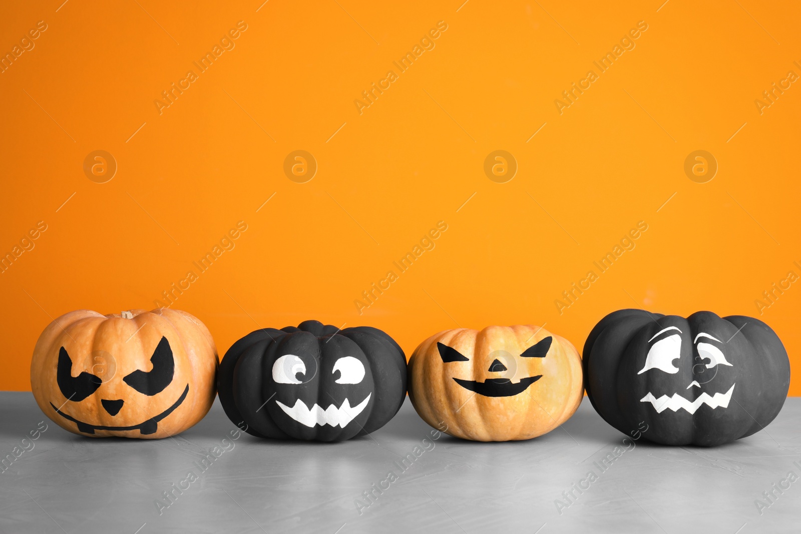 Photo of Pumpkins with scary faces on table against color background, space for text. Halloween decor