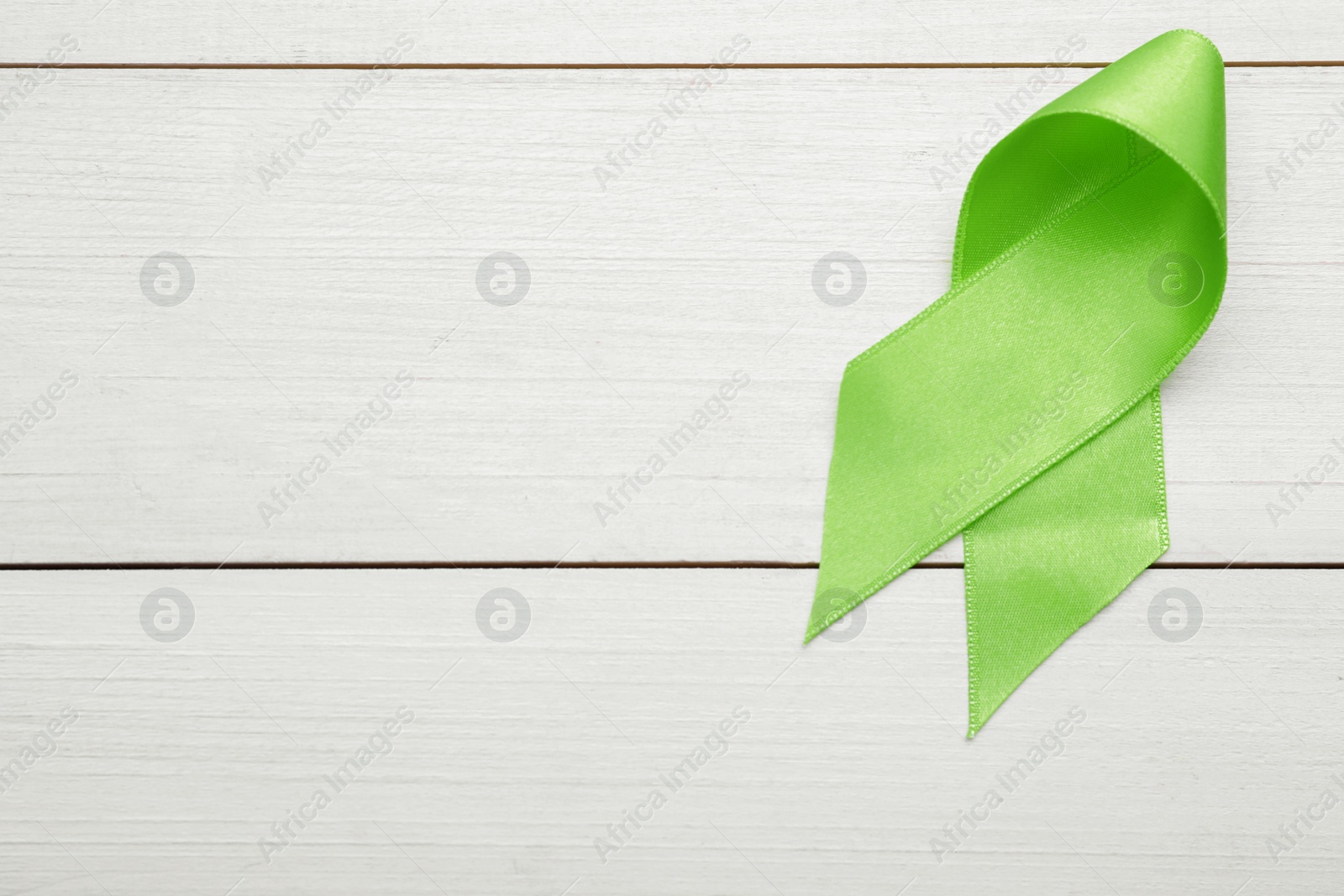 Photo of World Mental Health Day. Green ribbon on white wooden background, top view with space for text