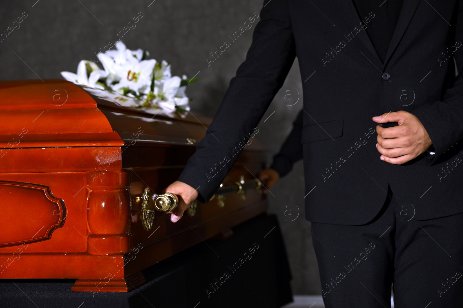 Photo of Young man carrying wooden casket in funeral home, closeup