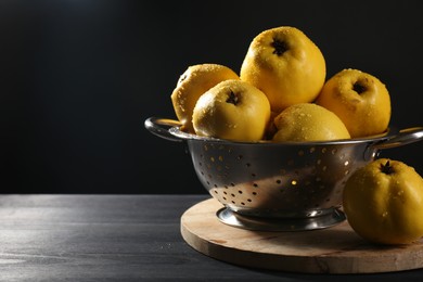Tasty ripe quinces with water drops in metal colander on black wooden table, closeup. Space for text