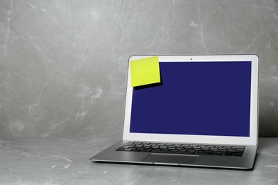 Laptop with blank sticky note on grey table. Space for text