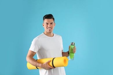 Photo of Handsome man with yoga mat and bottle on turquoise background