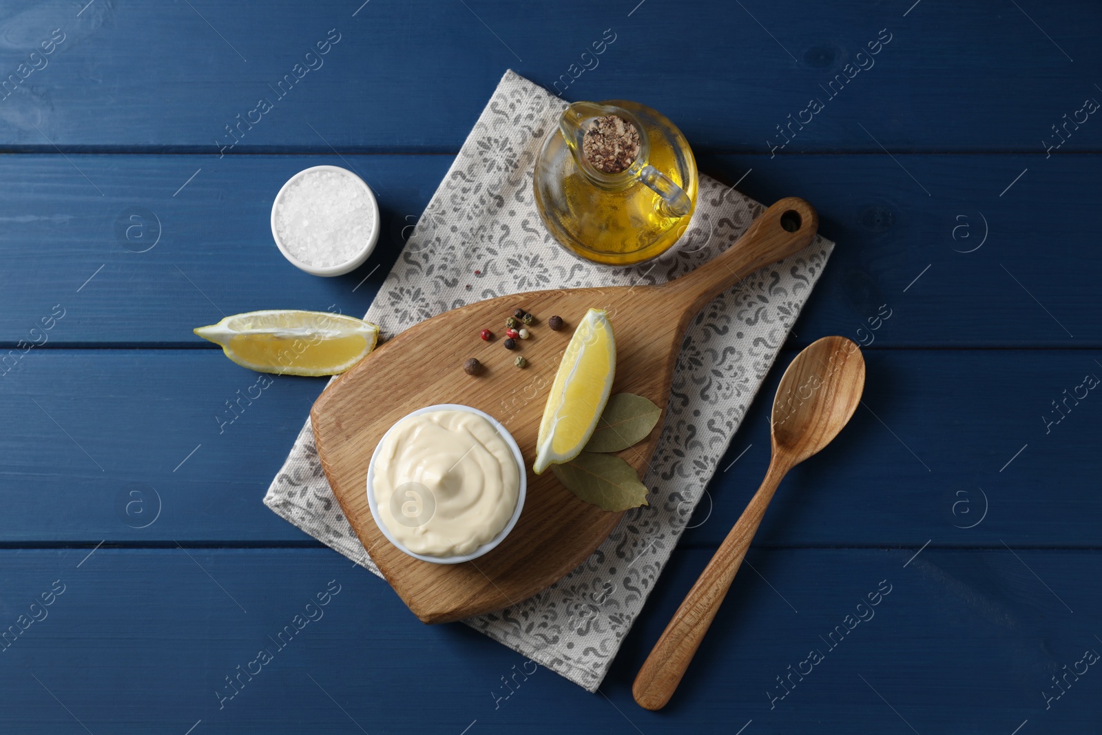 Photo of Tasty mayonnaise in bowl, products and spoon on blue wooden table, flat lay