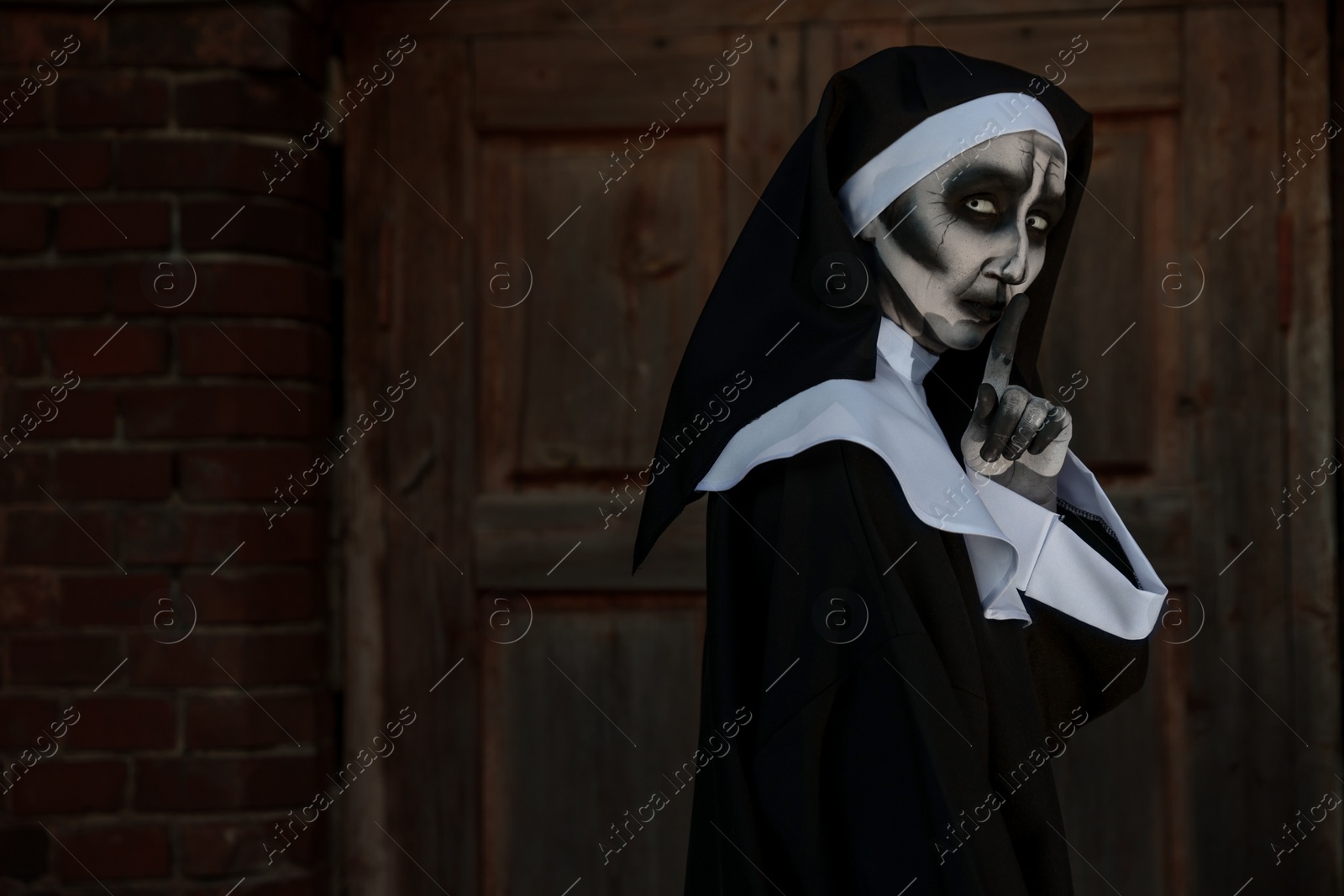 Photo of Portrait of scary devilish nun near red brick wall, space for text. Halloween party look