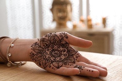 Woman with henna tattoo on palm at table indoors, closeup. Traditional mehndi ornament
