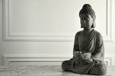Photo of Buddha statue on white marble table. Space for text