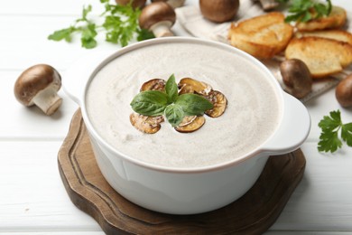 Delicious homemade mushroom soup in ceramic pot, croutons, fresh champignons and parsley on white wooden table