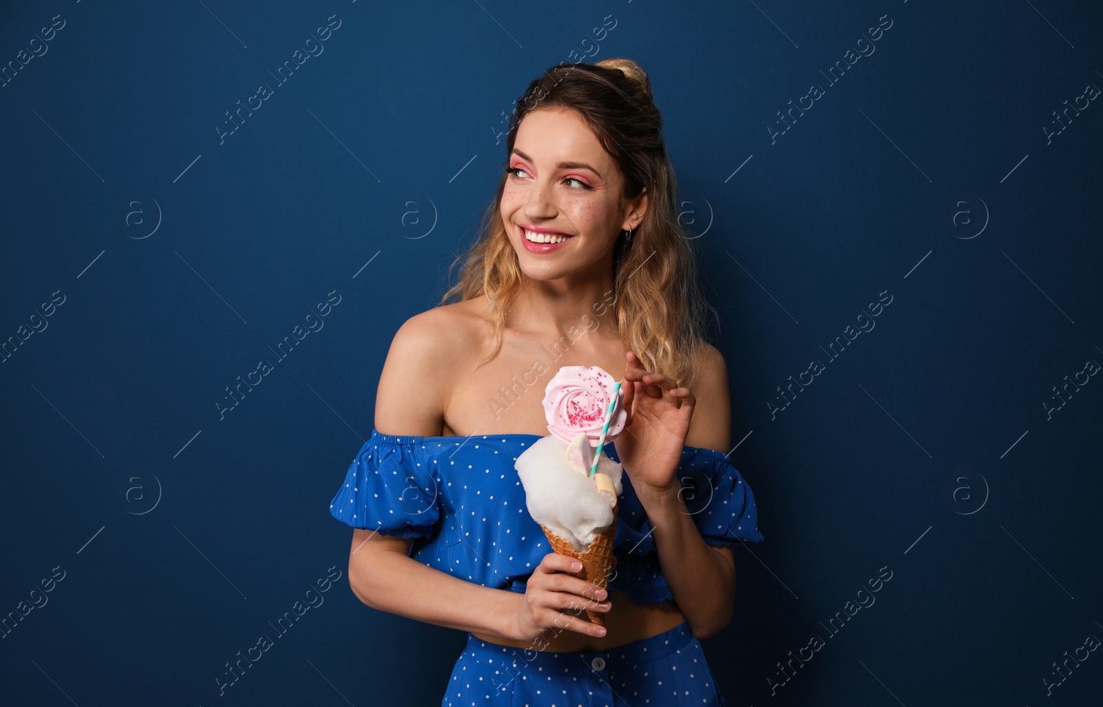 Photo of Portrait of young woman holding cotton candy dessert on blue background