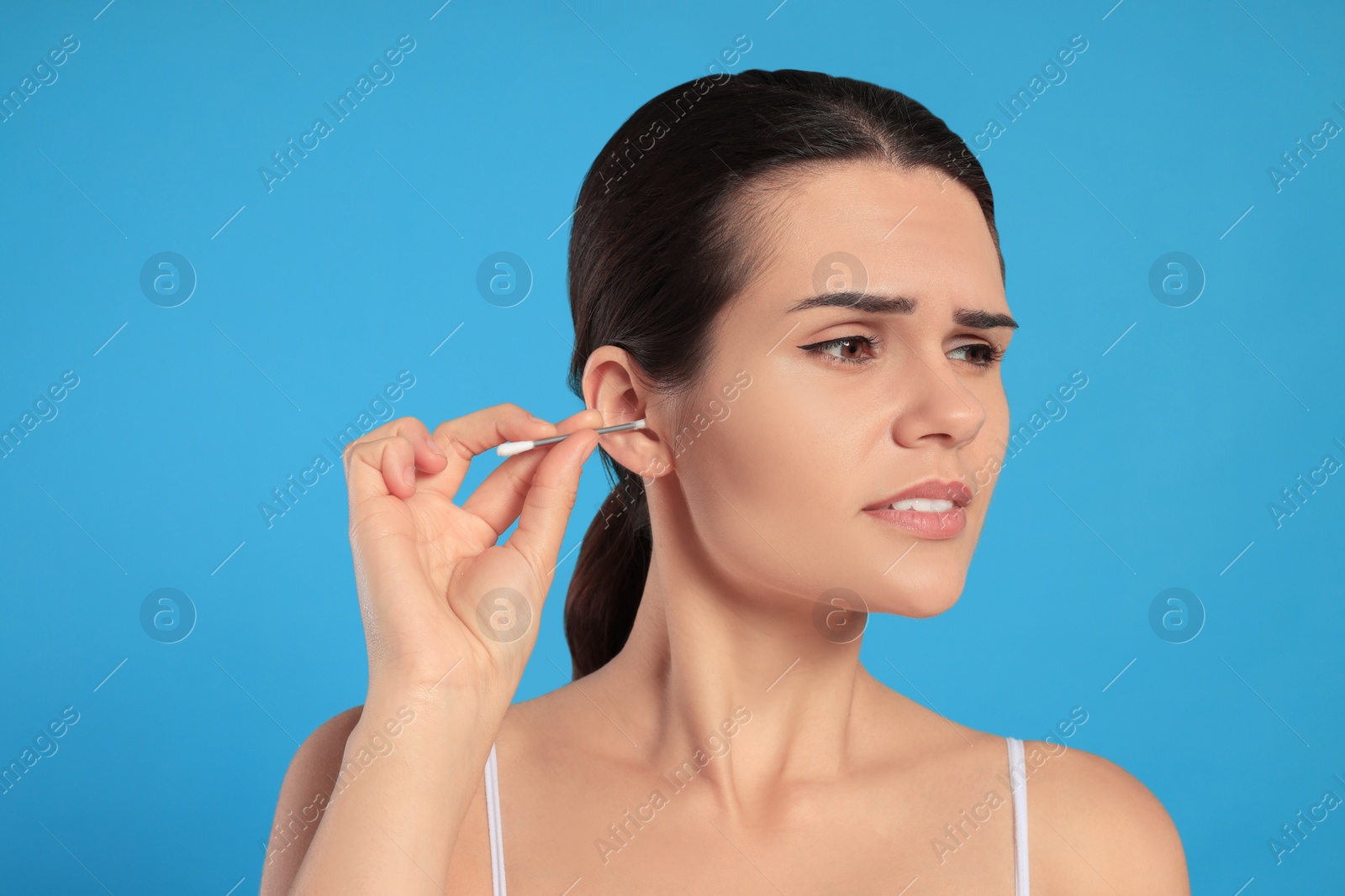 Photo of Young woman cleaning ear with cotton swab on light blue background