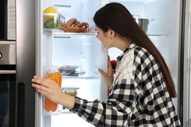 Young woman near modern refrigerator in kitchen