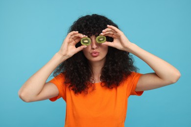 Photo of Woman covering eyes with halves of kiwi on light blue background