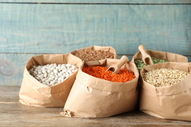 Photo of Different grains and cereals in paper bags on wooden table