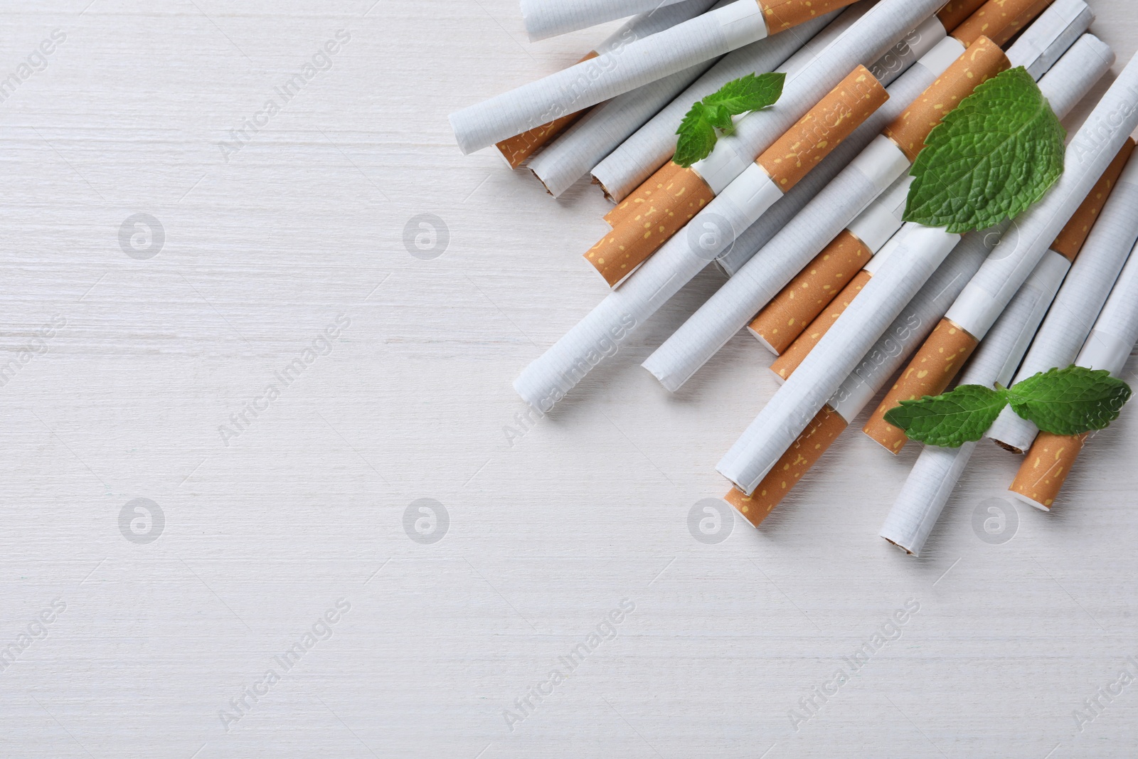 Photo of Menthol cigarettes and mint on white wooden table, flat lay. Space for text