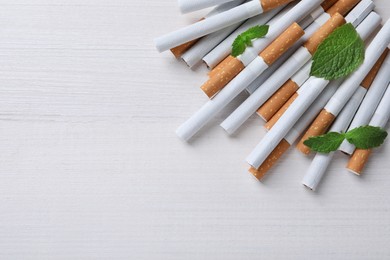 Photo of Menthol cigarettes and mint on white wooden table, flat lay. Space for text