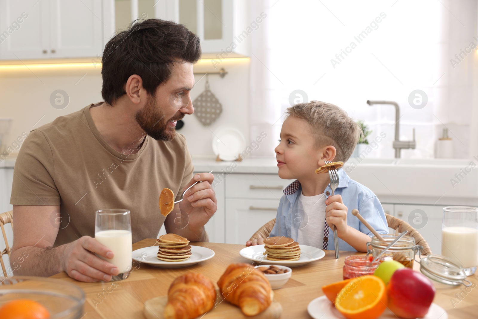 Photo of Father and his cute little son having breakfast at table in kitchen