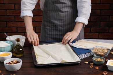 Woman making delicious baklava at wooden table, closeup