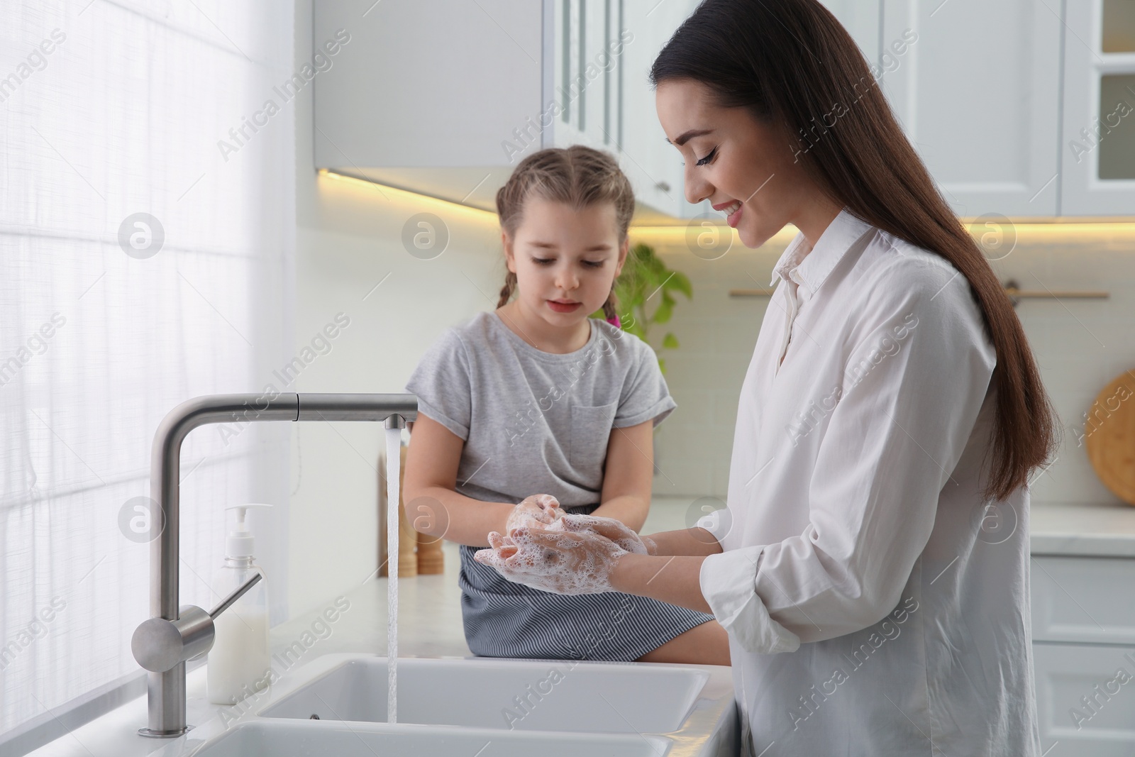 Photo of Mother and daughter washing hands with liquid soap in kitchen