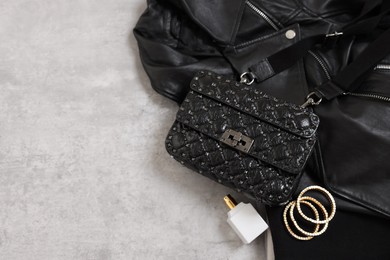 Bag, black leather jacket, bottle of perfume and golden bracelets on grey table, above view. Space for text