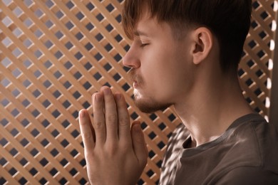 Photo of Man praying during confession near wooden window in booth, closeup