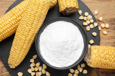 Bowl with corn starch, ripe cobs and kernels on wooden table, flat lay