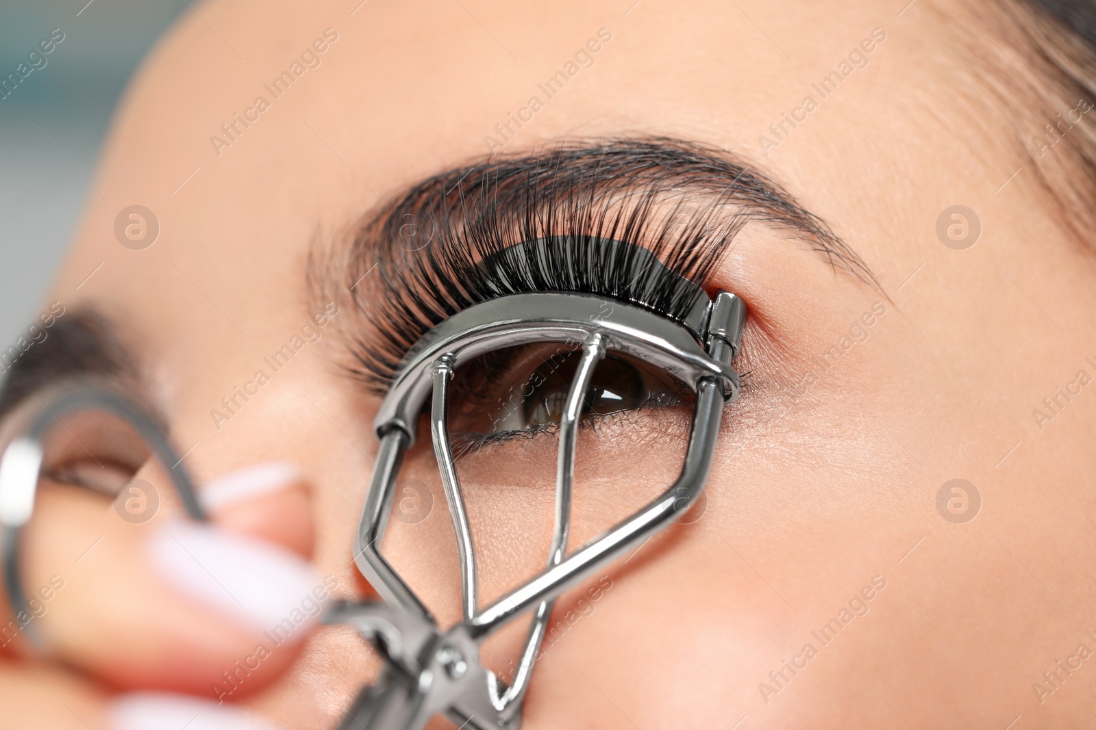 Photo of Young woman using eyelash curler on grey background, closeup